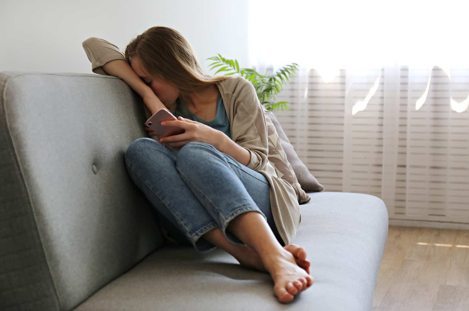 photo d'une jeune femme déprimée cachant son visage assise sur un canapé gris tenant le téléphone