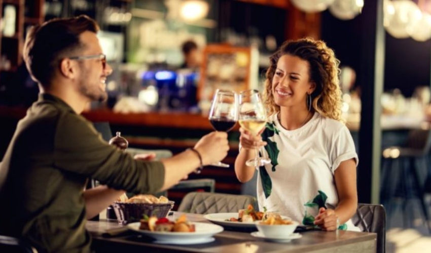 Jeune couple heureux celebrant et portant un toast avec des verres a vin tout en mangeant dans un restaurant.