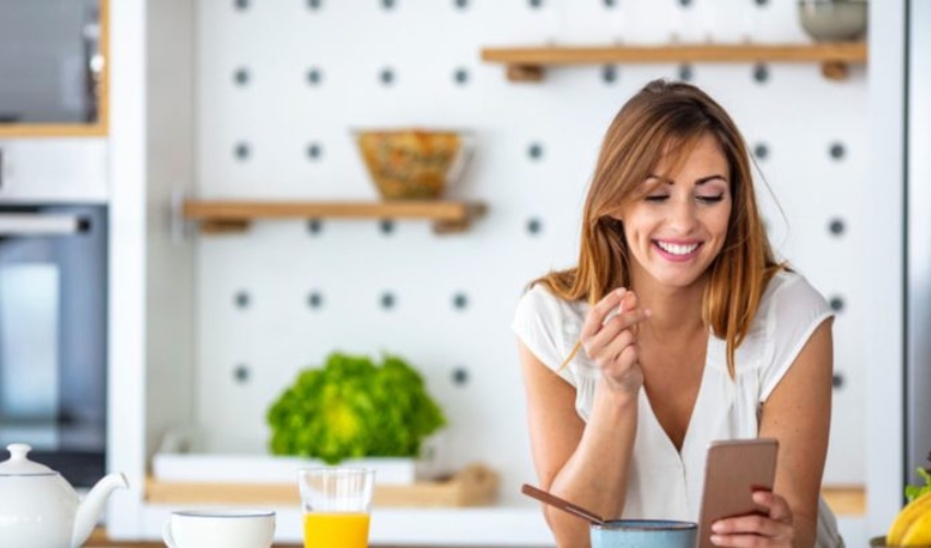 femme heureuse envoyant des SMS dans la cuisine