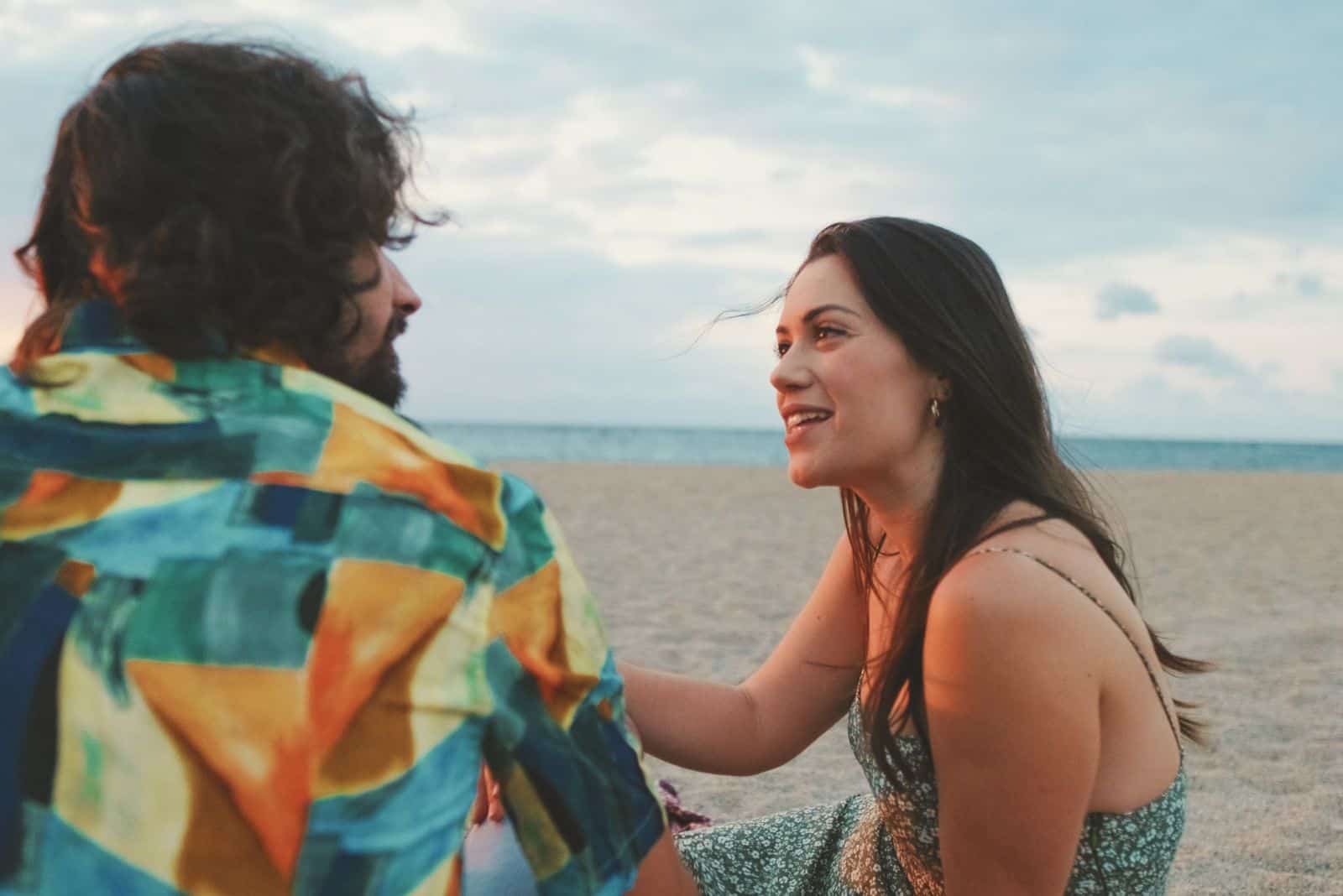 un couple d'amoureux est assis sur la plage et parle