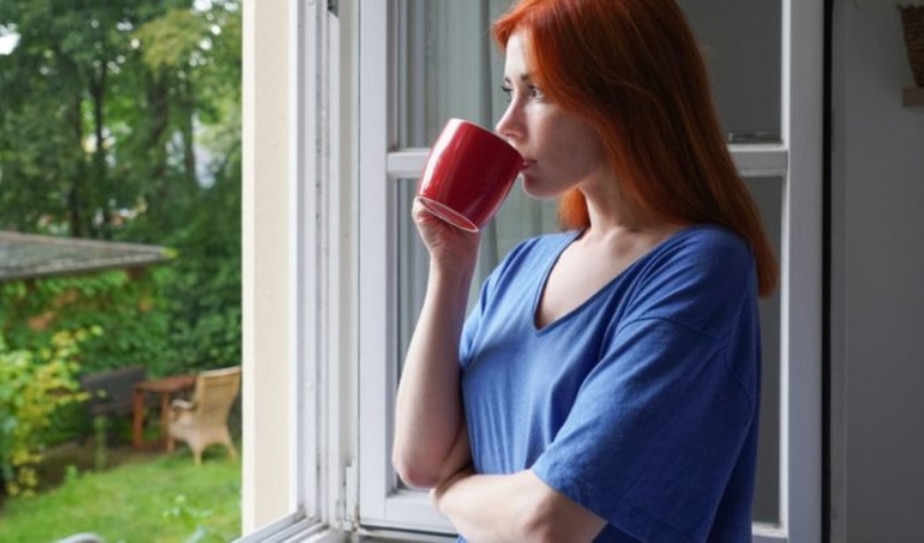 jeune femme debout pres dune fenetre ouverte buvant du cafe