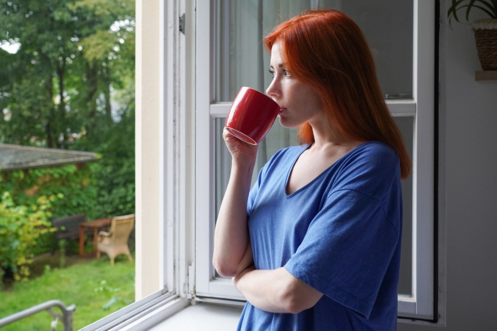 jeune femme debout près d'une fenêtre ouverte buvant du café