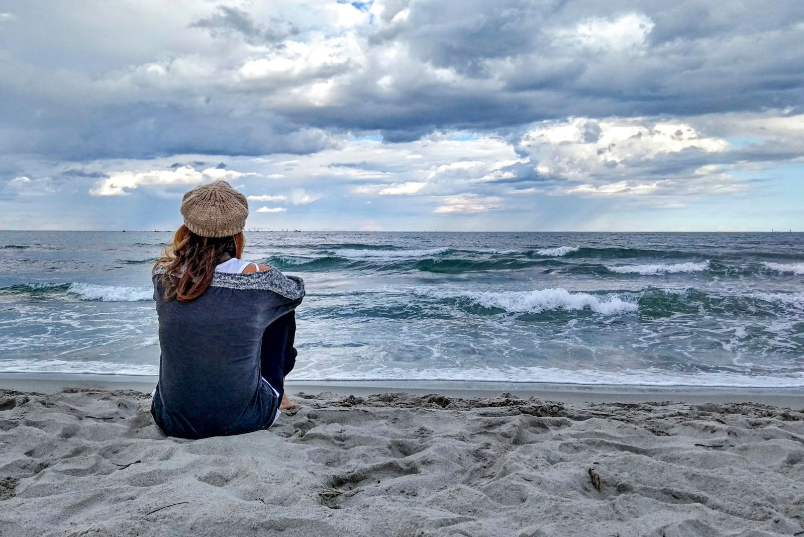 Jeune femme assise au bord de la mer avec un ciel orageux, regarde pensivement l'horizon