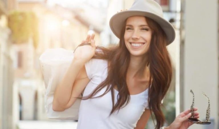 une femme avec un chapeau et des lunettes a la main rit