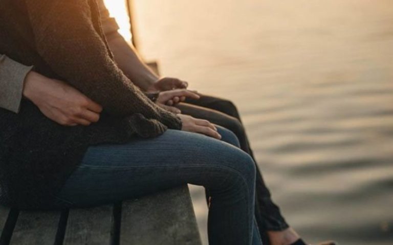 un homme et une femme sont assis sur un mur au bord de la mer