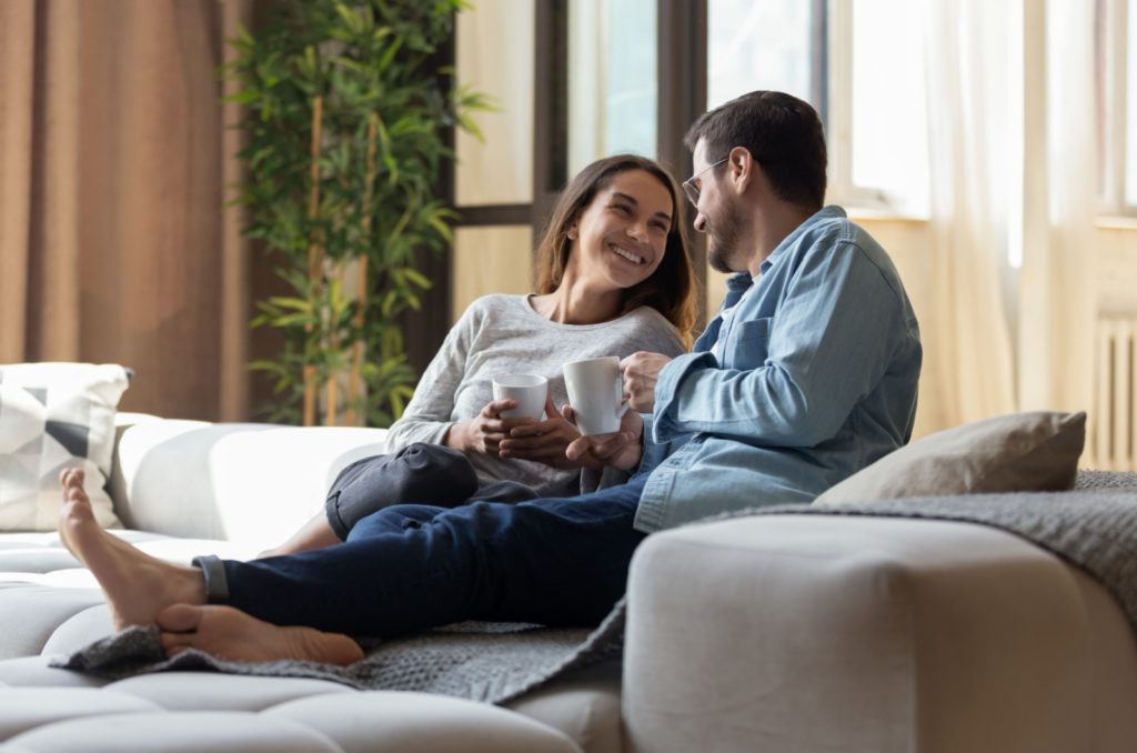 couple aimant souriant assis sur un canapé buvant du café