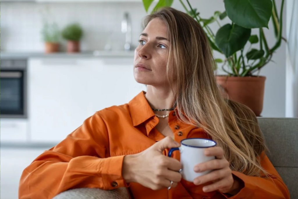 la jeune fille est pensive sur le canapé, tenant une tasse à la main